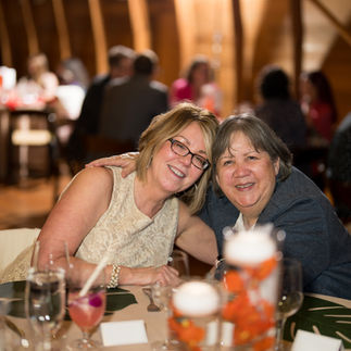 Two smiling women embracing at a warm, festive event reception.