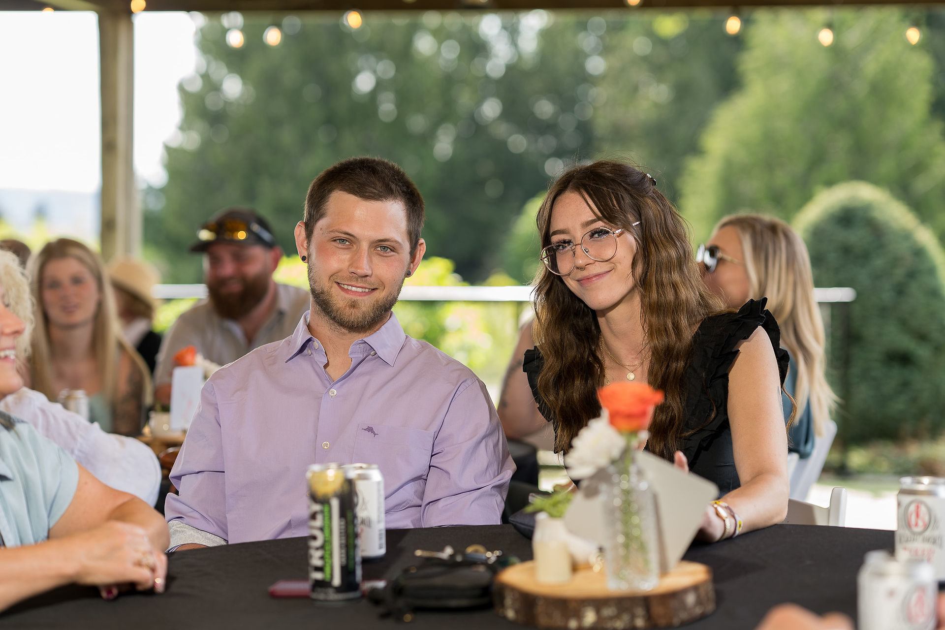 Smiling man and woman at outdoor table with TRULY drinks, flowers.