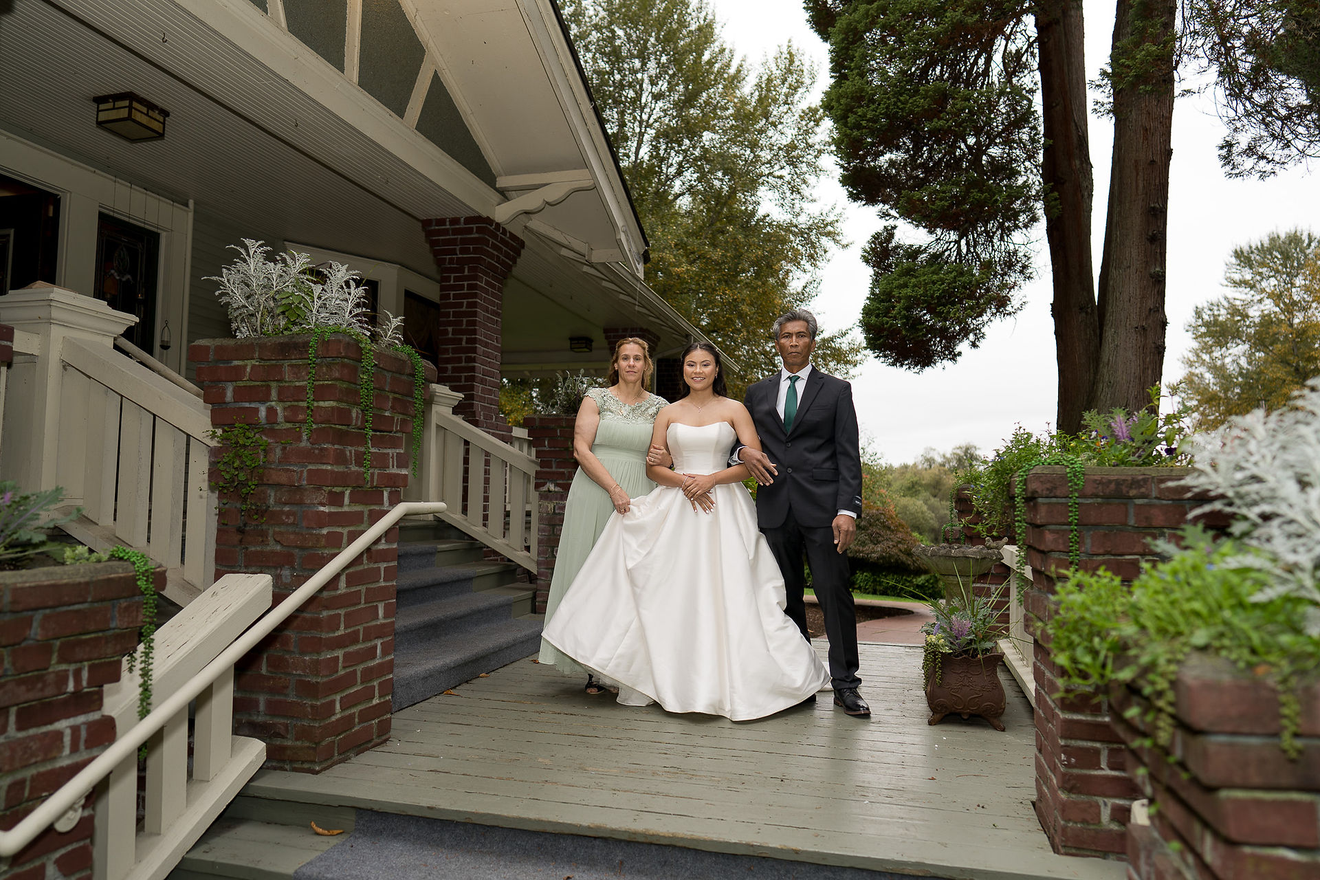Bride with parents posing outside a charming wedding venue.