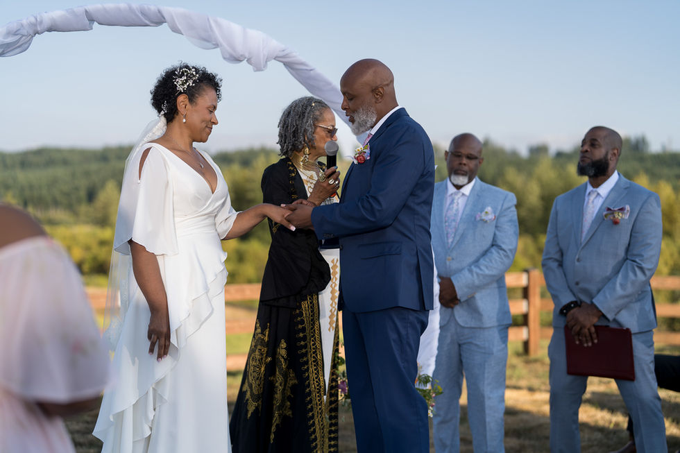 Happy couple exchanging vows outdoors with officiant at their wedding.