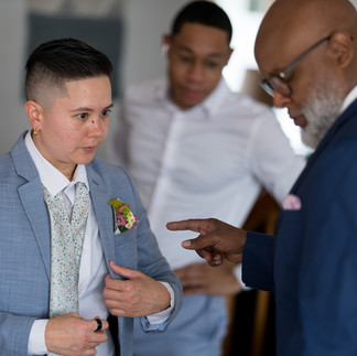 Stylish person in blue suit adjusts jacket, older man advises.