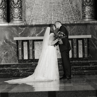 Bride and groom embrace and kiss at ornate chapel altar.