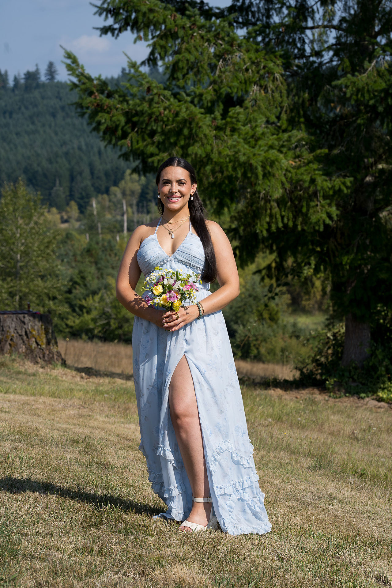 Smiling woman in light blue dress holding colorful bouquet outdoors.