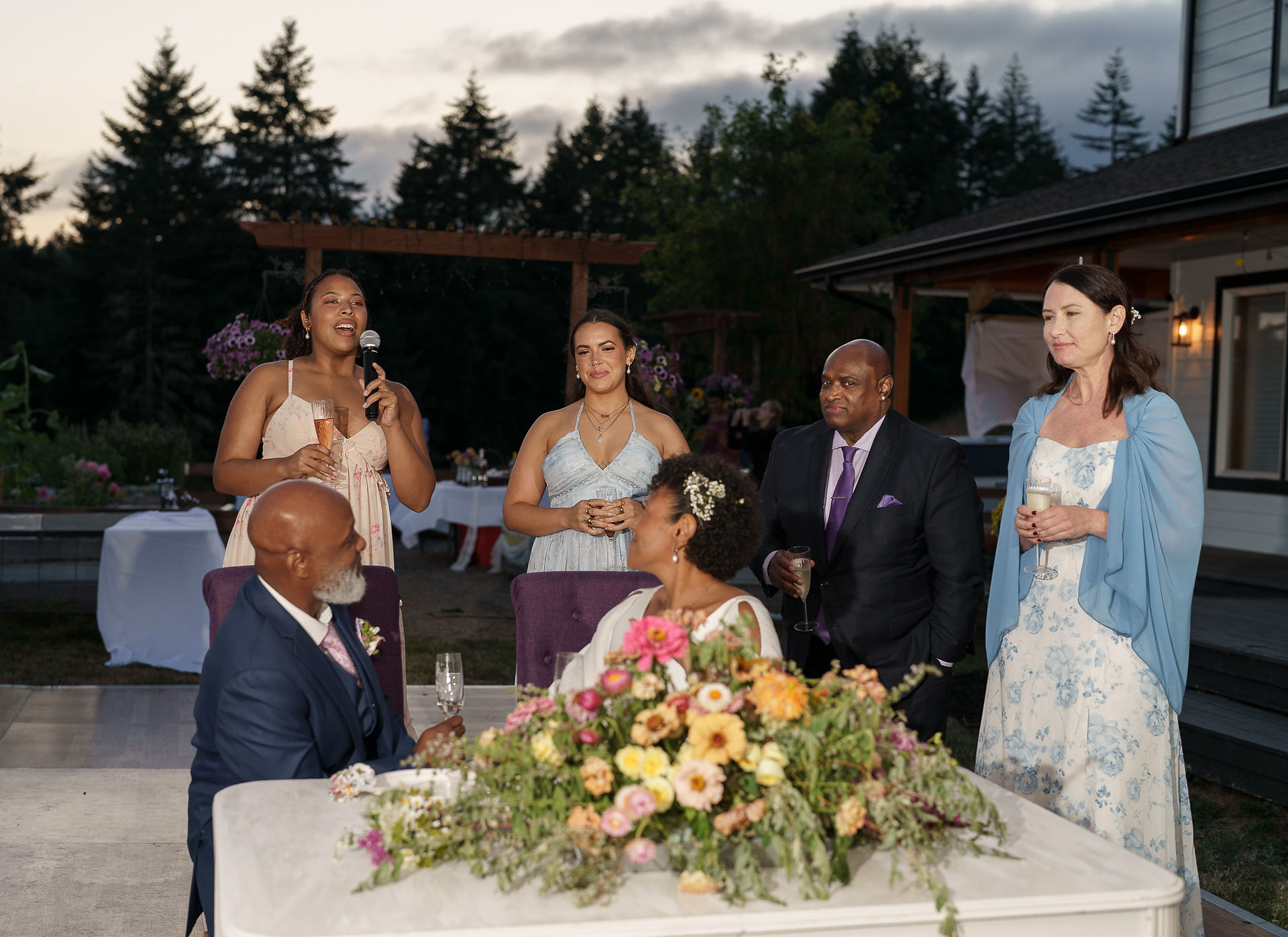 Woman giving speech to wedding couple and guests at outdoor reception.