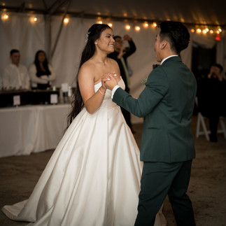 Happy bride and groom dancing under string lights at wedding reception.