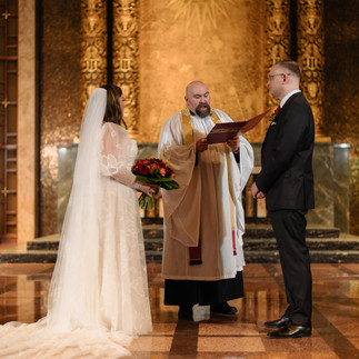 Bride and groom exchanging vows with a priest in a golden chapel.
