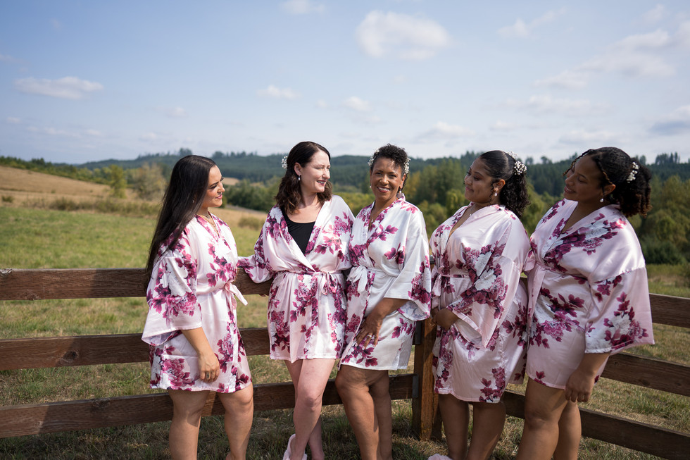Bridal party in floral robes posing happily at outdoor farm setting.