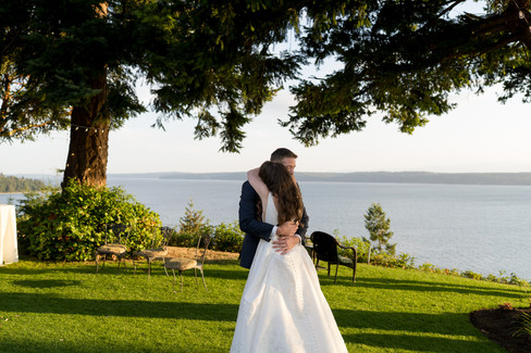 Bride and groom embrace at outdoor wedding overlooking ocean.
