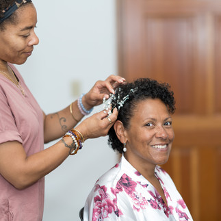 Stylist adds decorative hairpiece to smiling bride's short curly hair.