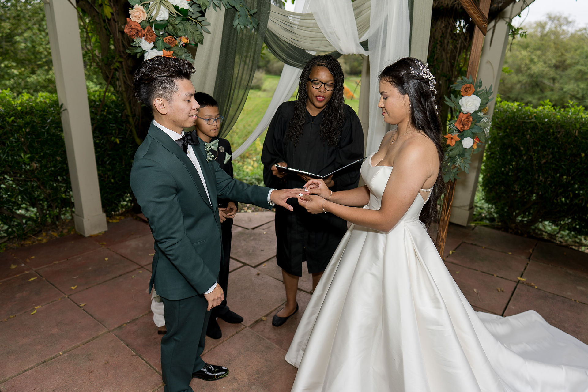 Groom places ring on bride's finger during their outdoor wedding ceremony.