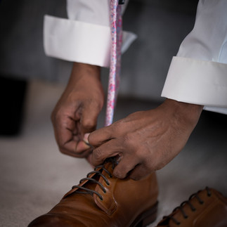 Hands tying laces on tan leather dress shoes, measuring tape visible.