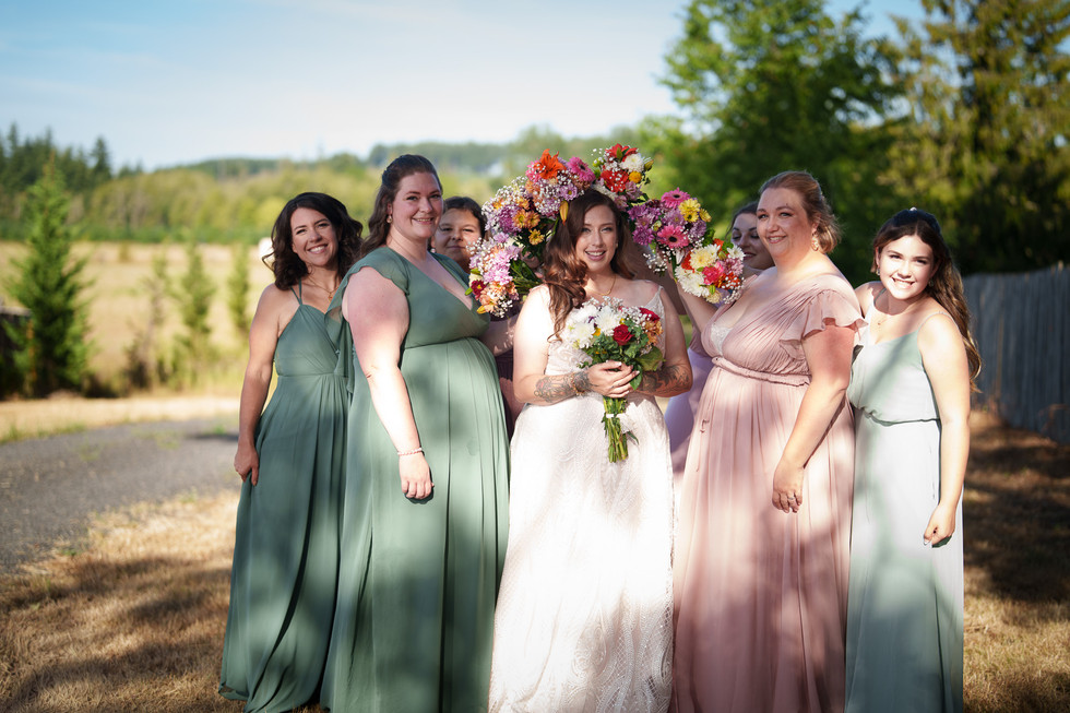 Bride and bridesmaids smiling outdoors, holding colorful bouquets.