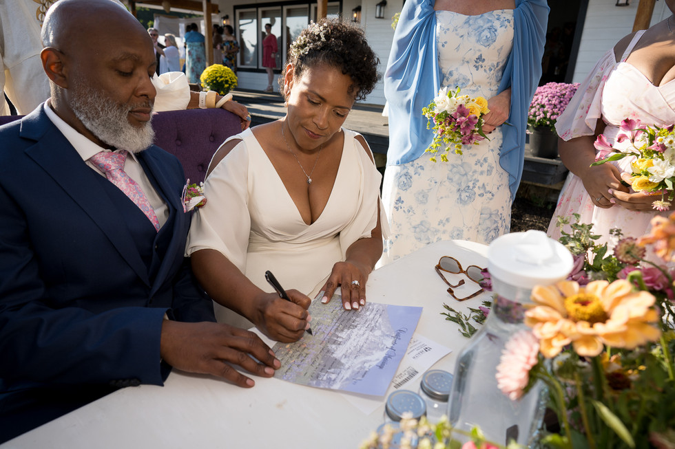 Bride in white dress signing marriage license at intimate farm wedding.