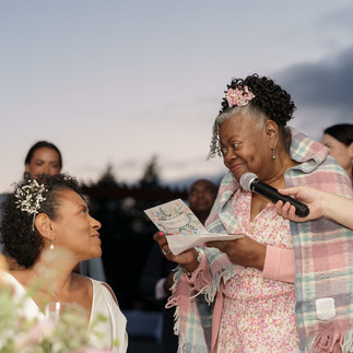 Smiling older woman holds microphone, gives speech to bride.