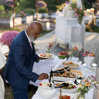 Man in suit serving food from outdoor wedding buffet table.