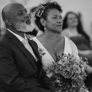 Bearded man and woman intently watching ceremony, she holds bouquet.