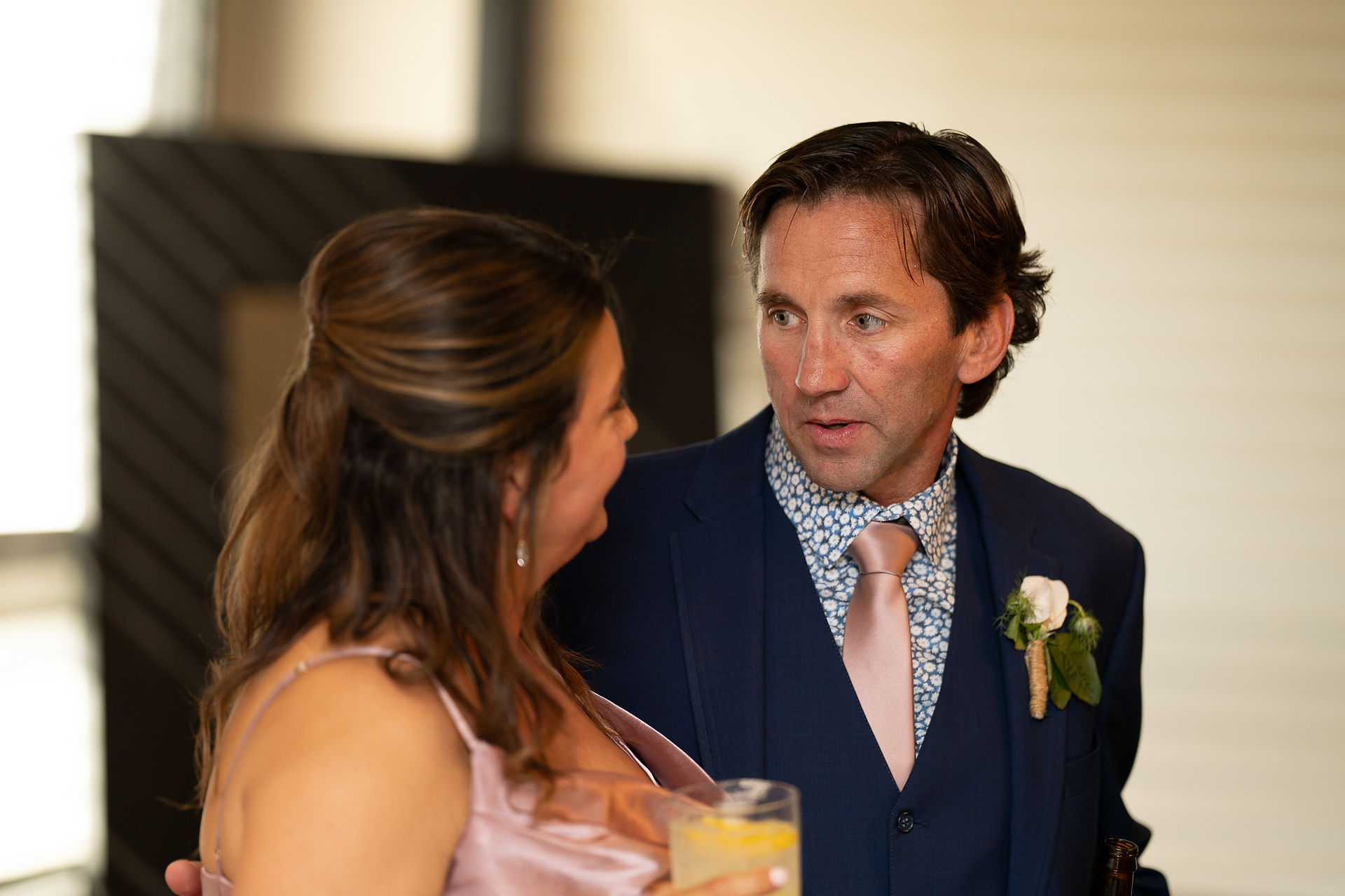 Wedding guest man in suit conversing with woman holding a drink.