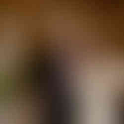 Smiling bride and groom stand by wedding cake at reception.