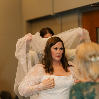 Bride in white dress getting veil adjusted by helper.
