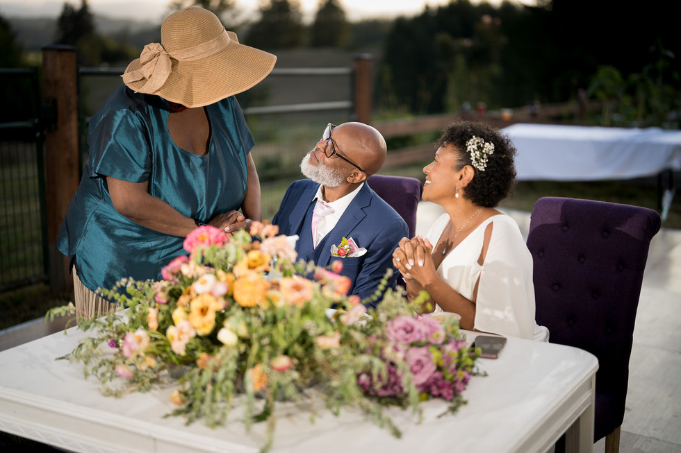Joyful couple at intimate farm wedding, speaking with a guest.