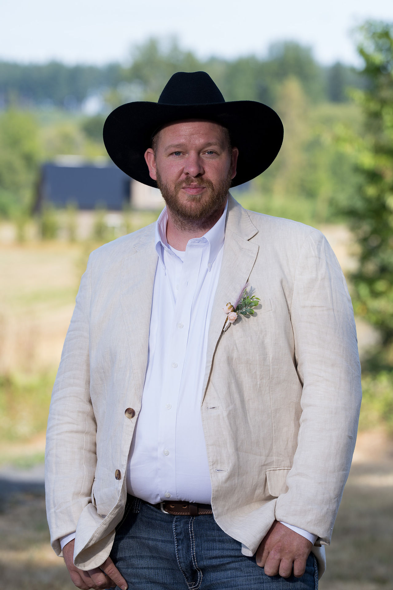 Man in black hat, linen jacket, and boutonniere outdoors.