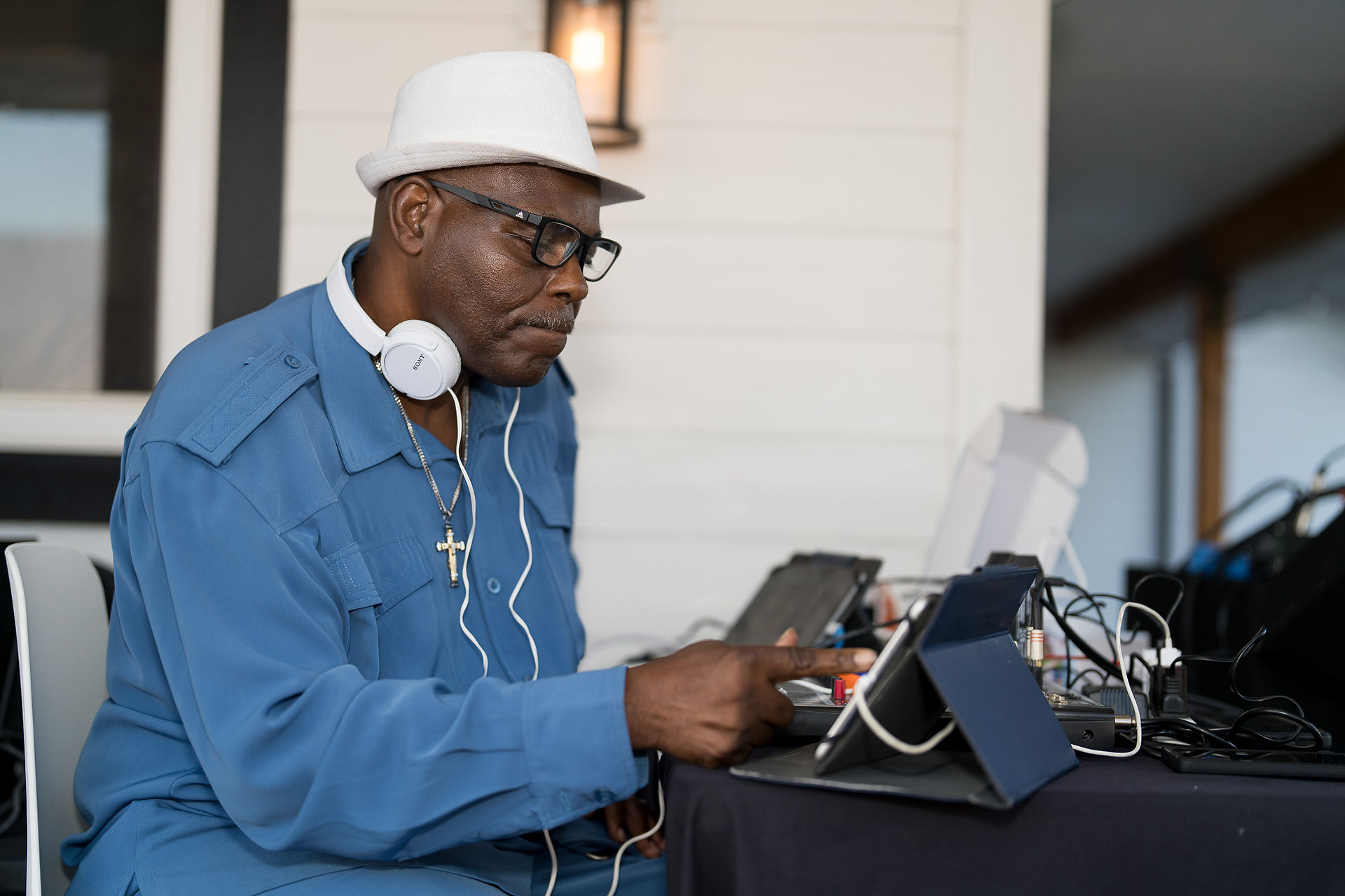 DJ wearing headphones and white hat operating tablet with stylus.