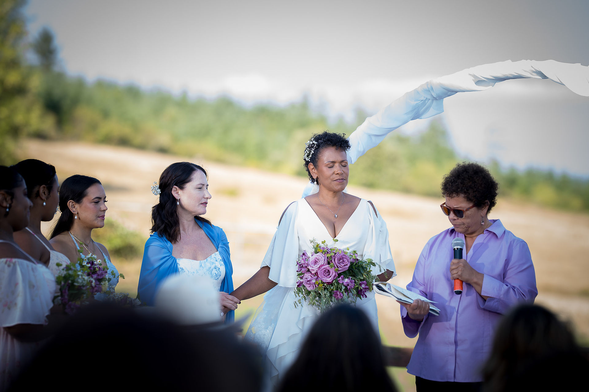 Diverse couple holds hands during intimate farm wedding ceremony outdoors.