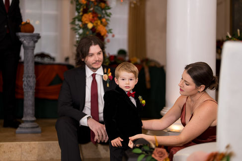 Man, boy in velvet suit, woman in rust dress at fall wedding.