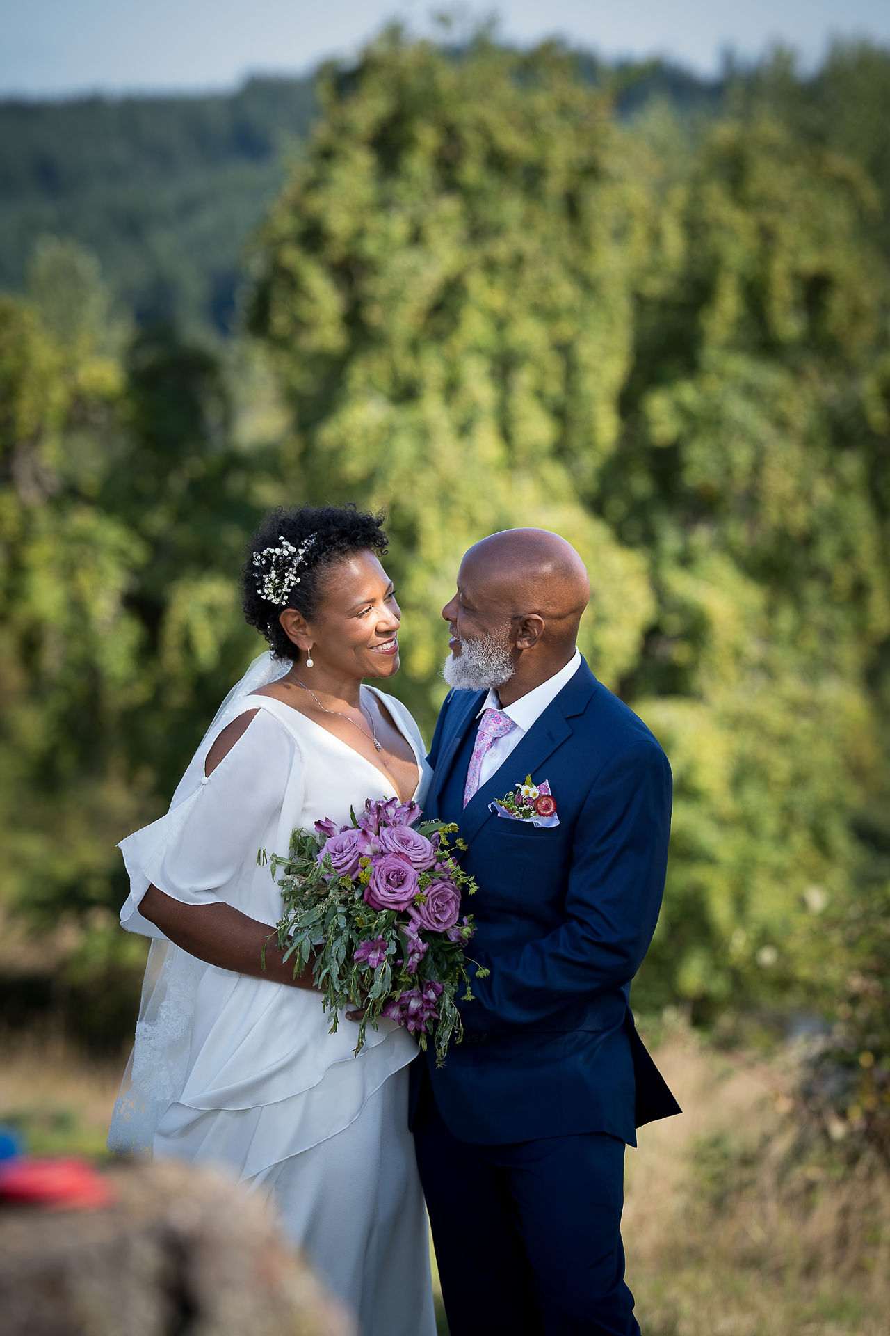 Smiling Black wedding couple gazing lovingly, bride holding purple bouquet.