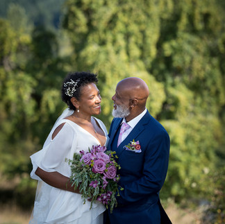 Smiling Black wedding couple gazing lovingly, bride holding purple bouquet.