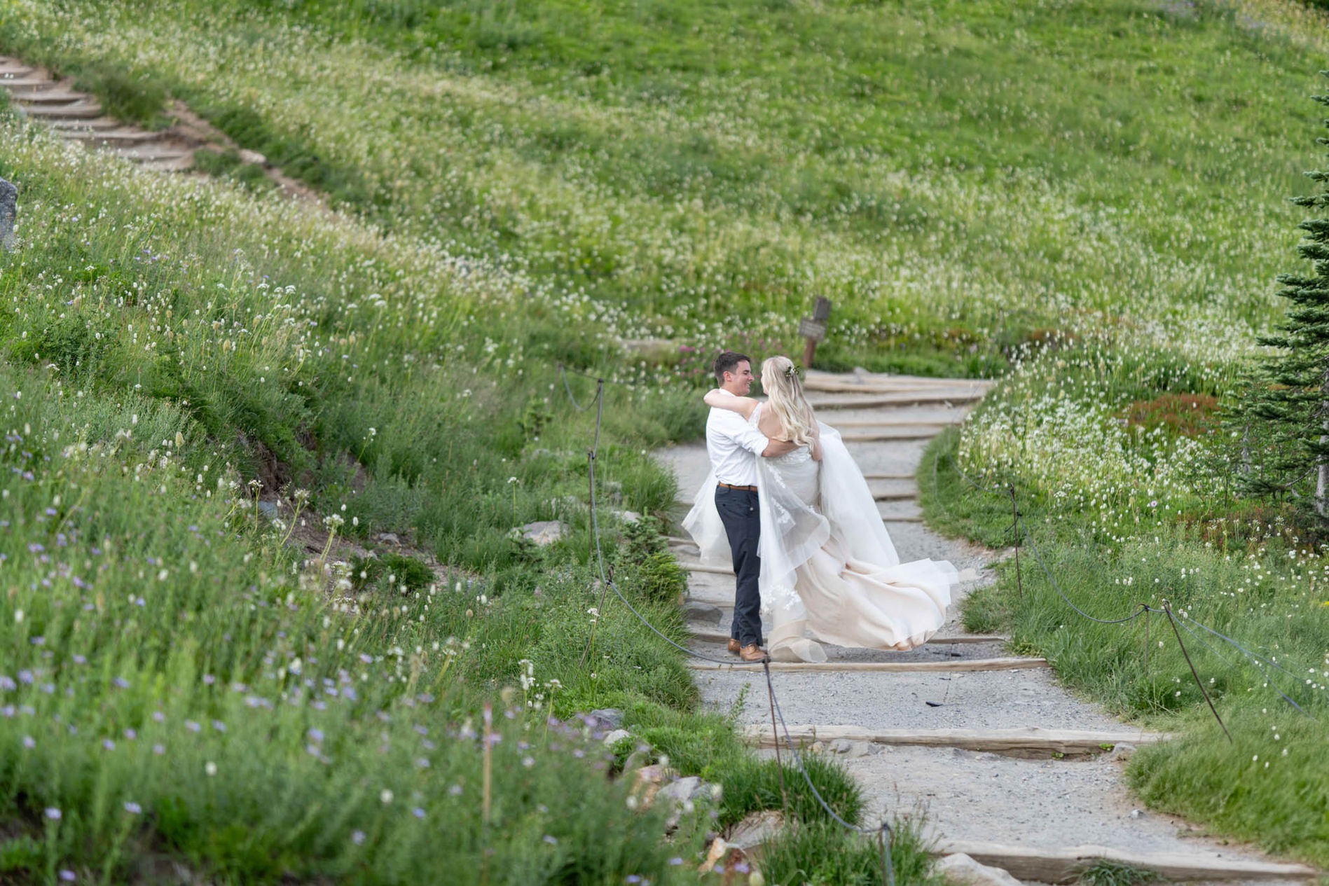 Couple embracing on stone steps, surrounded by green hillside foliage.