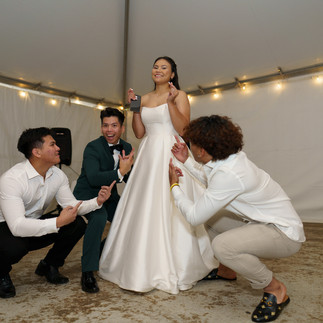 Bride in white gown holding microphone, three friends playfully pointing.