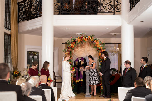 Couple at elegant indoor fall wedding ceremony under floral arch.