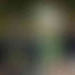 Groom in green suit smiles with family at outdoor wedding gazebo.