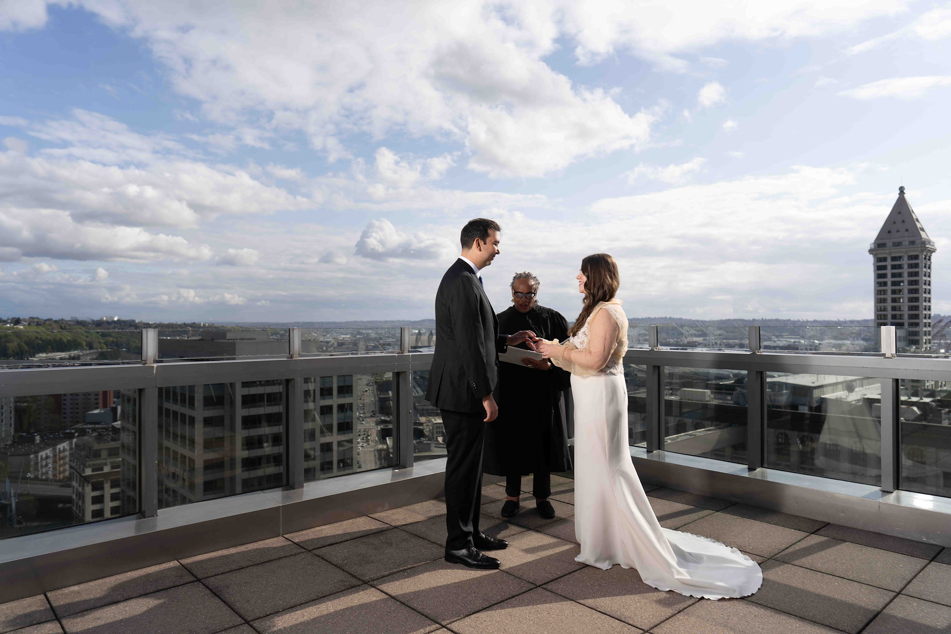 Couple exchanging vows rooftop ceremony, Seattle skyline