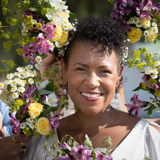 Smiling woman with curly hair adorned with colorful flowers.