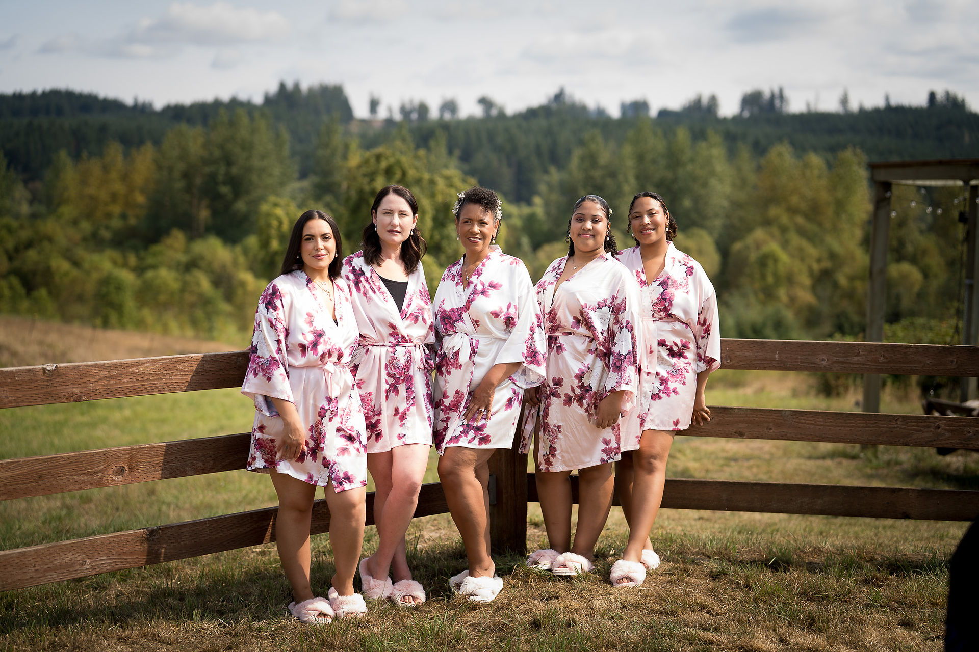 Five women in matching floral robes standing outdoors by a fence.