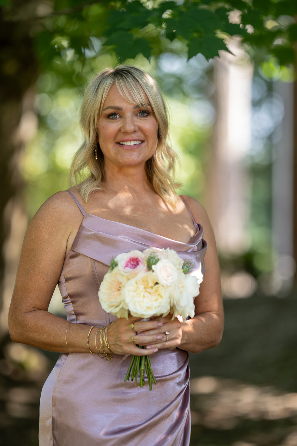 Smiling woman in lilac dress holding white and pink rose bouquet outdoors.