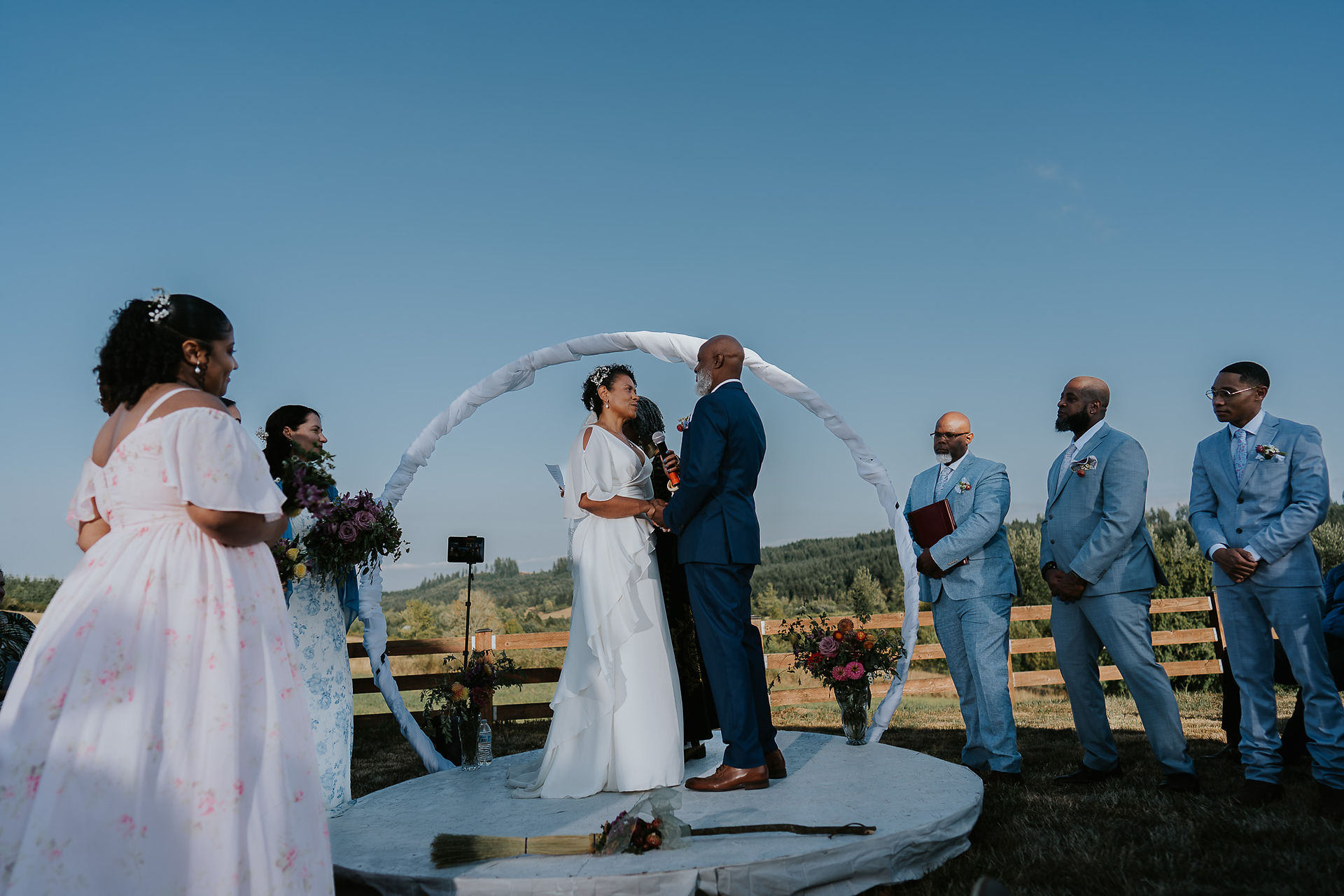 Bride and groom marry under white arch at intimate farm wedding.