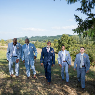 Groomsmen in blue suits walking across a sunny farm field.