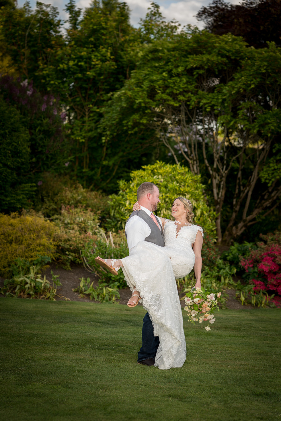 Groom lifts smiling bride in elegant wedding dress at Olympic View Estates.