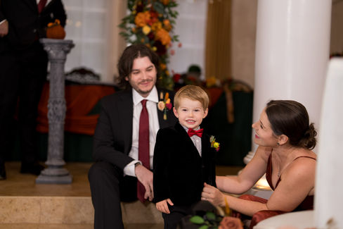 Smiling man, young boy in velvet suit at a warm autumn wedding.