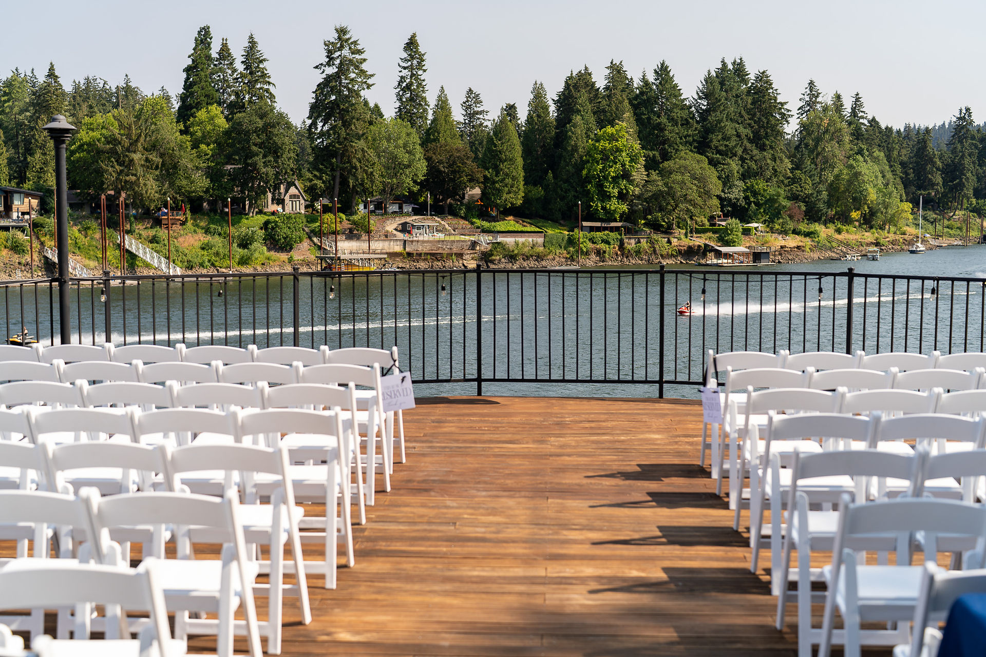 White chairs on wooden deck overlooking water for a wedding ceremony.