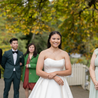 Smiling bride in white gown outdoors with wedding party behind.