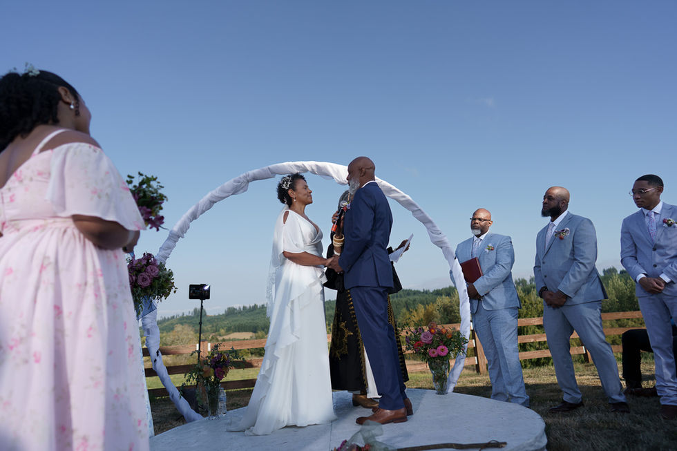 Couple exchanges vows outdoors under a white floral arch.