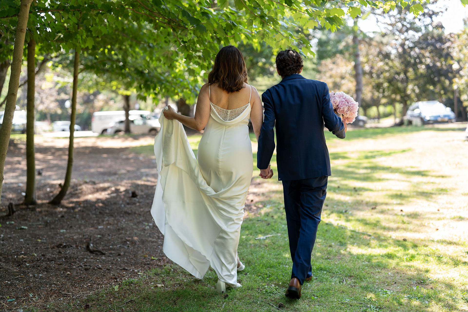 Newlyweds walking away hand-in-hand outdoors after their elegant summer wedding.