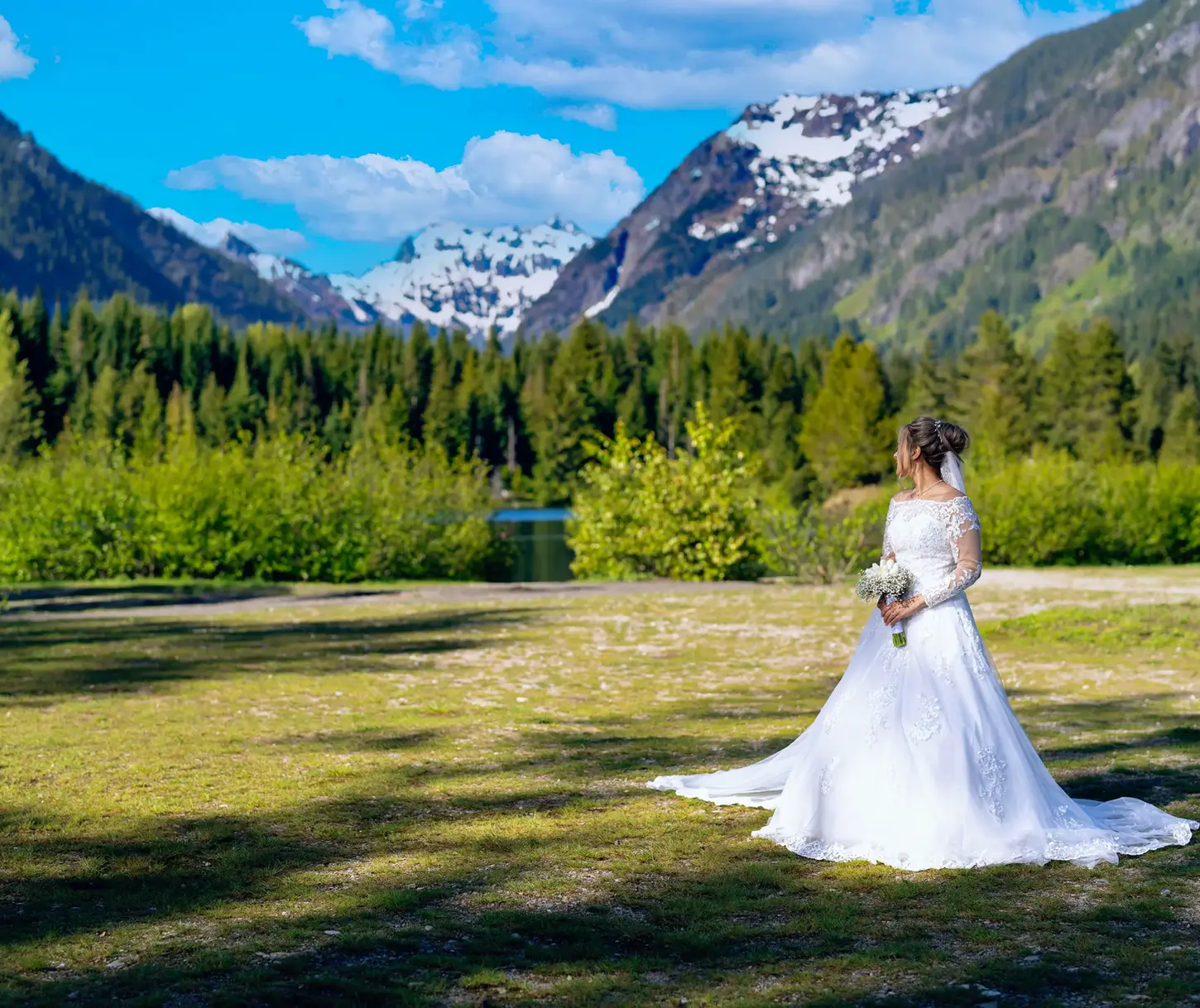 White-gowned bride, holding bouquet, snowy mountains, green forest, PNW wedding.
