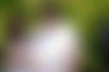 Groom in cowboy hat looking down, bride's arm, outdoor wedding.