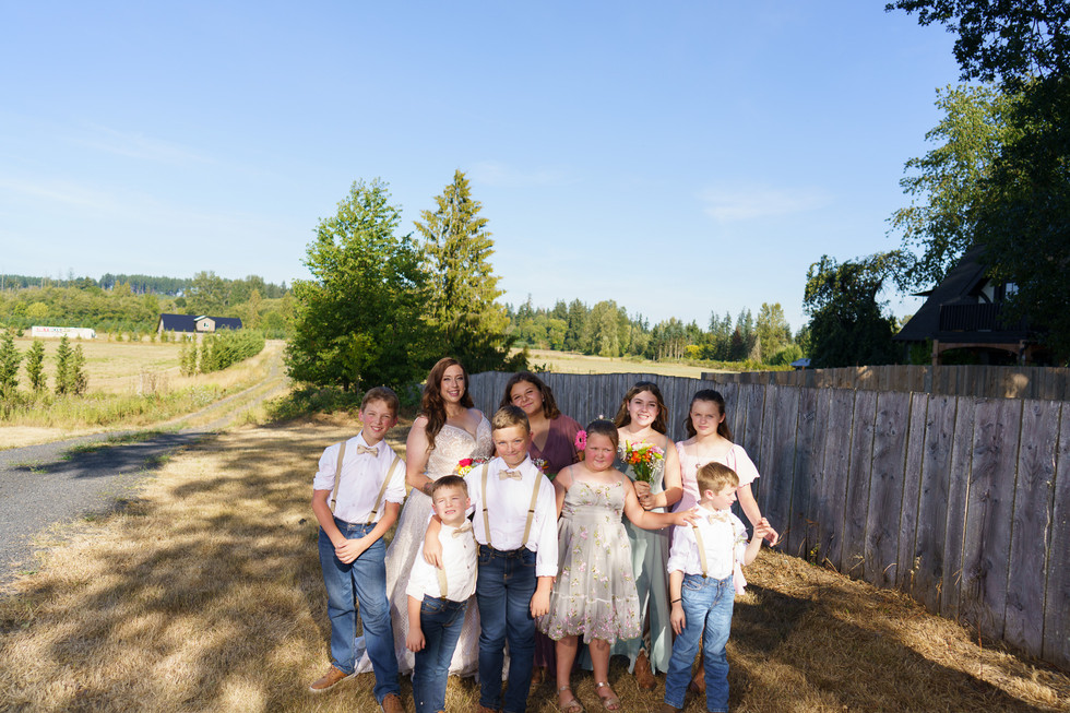 Smiling bridal party with children posed outdoors on a sunny day.