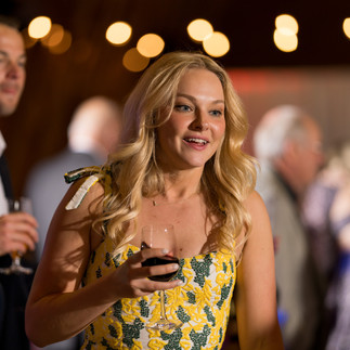 Smiling blonde woman in yellow dress holding wine glass at gathering.